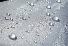 Water droplets of various sizes scattered on a smooth, reflective white surface, resembling beads on a radome.